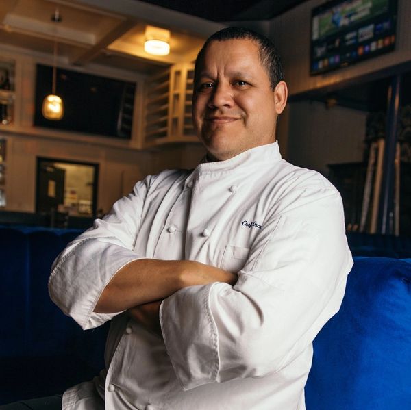 Confident chef in a white coat sitting with arms crossed in a cozy restaurant.