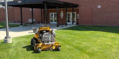 A lawn mower on green grass in front of Bishop Dubourg High School.