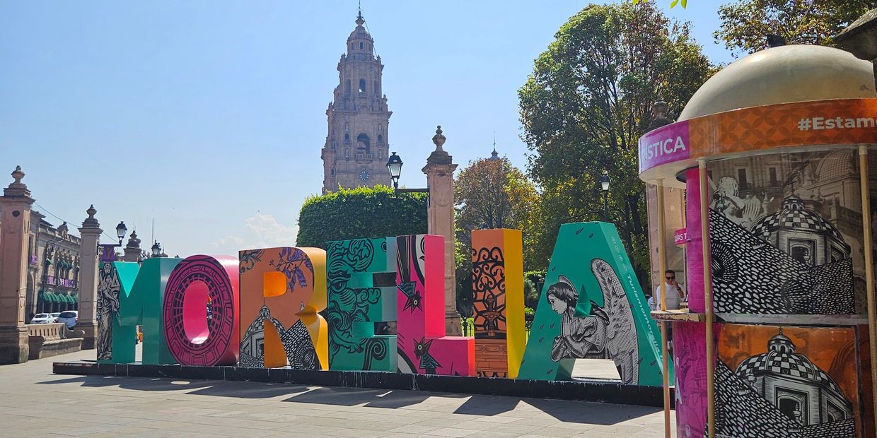 Colorful Morelia sign with a historic tower in the background on a sunny day.