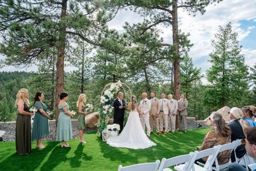 Outdoor wedding ceremony with bride, groom, bridal party, and guests in a forest setting.