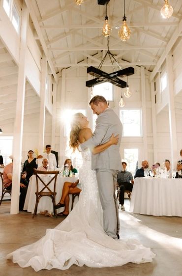Bride and groom share their first dance in a bright, rustic wedding venue.