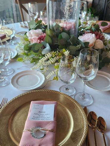 Elegant table setting with gold plate, pink napkin, and floral centerpiece.