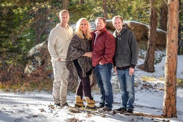 A group of four people smiling outdoors in a snowy forest.