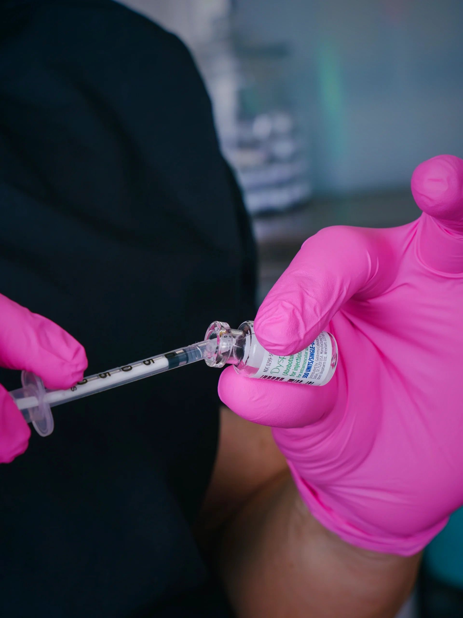 Picture of a provider wearing pink gloves drawing up Dysport into a syringe.