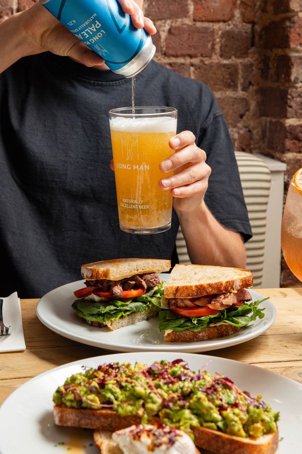 Person pouring local longman beer into a glass, steak sandwich sandwiches on the table.