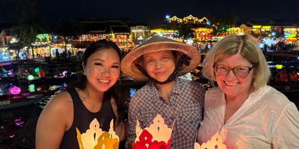 Three women smiling at a night festival with colorful lanterns.
