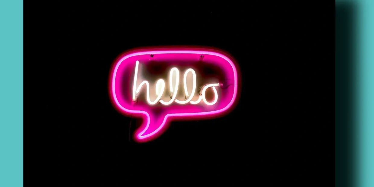 Neon sign spelling 'hello' inside a pink speech bubble on a black background.