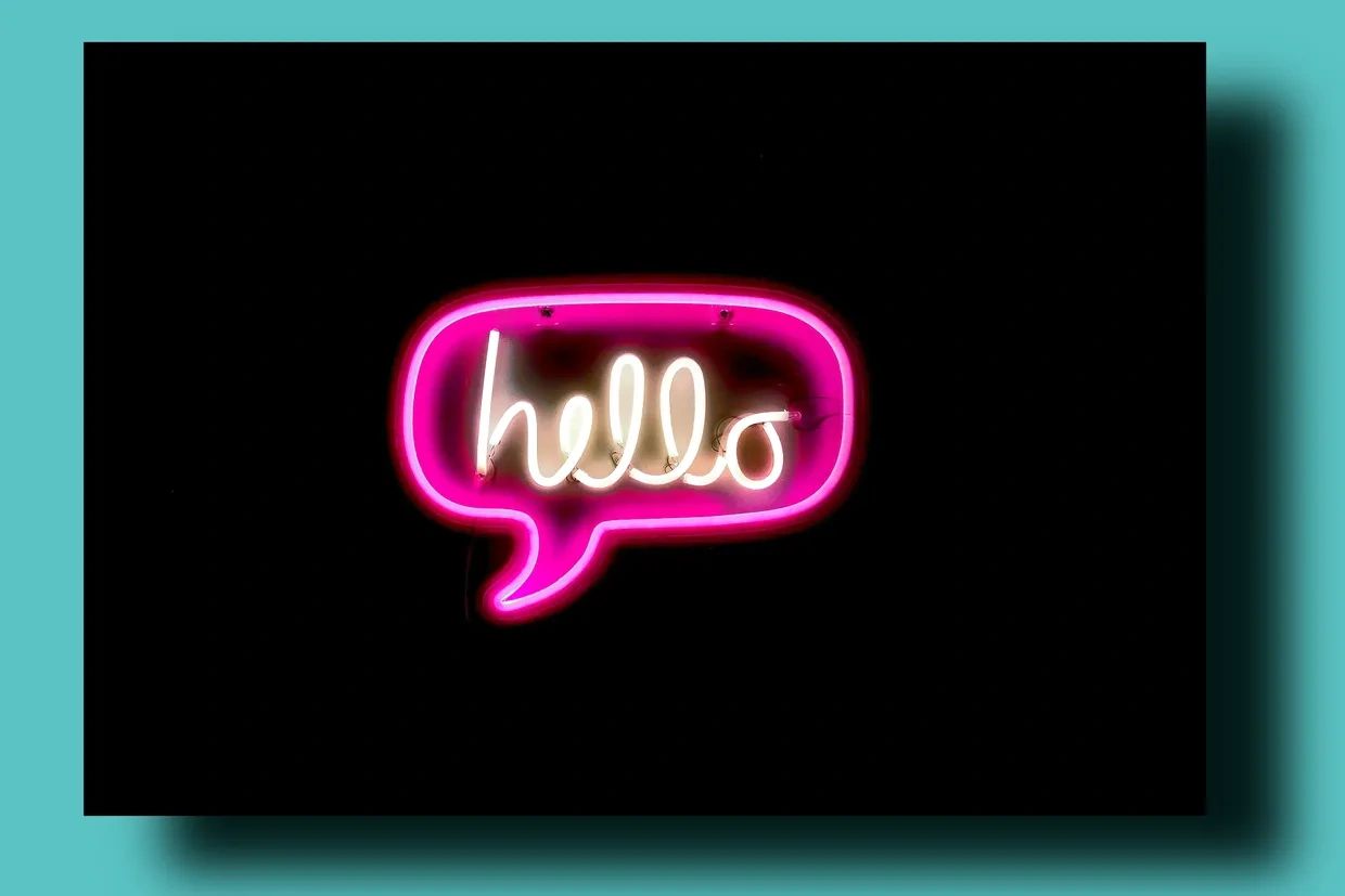 Neon sign spelling 'hello' inside a pink speech bubble on a black background.