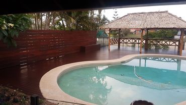 Poolside area with wooden deck and thatched gazebo.