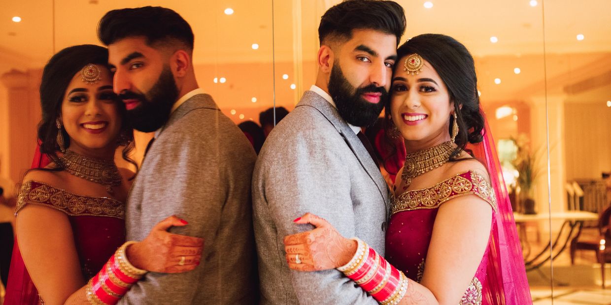 A couple in traditional attire embracing and smiling in front of a mirror.