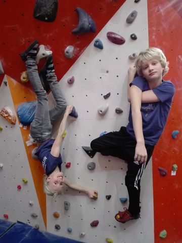 Two boys climbing an indoor rock wall, one upside down.