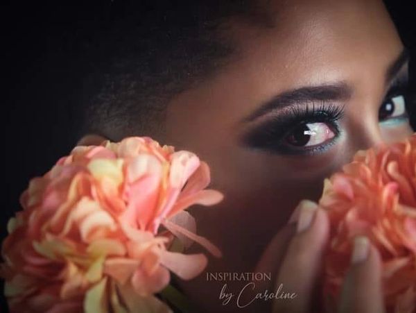 Close-up of a woman's eye peeking through peach-colored flowers.