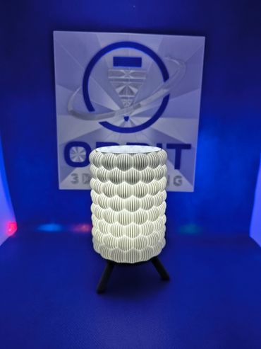 Glowing textured cylindrical lamp on tripod stand with blue background.