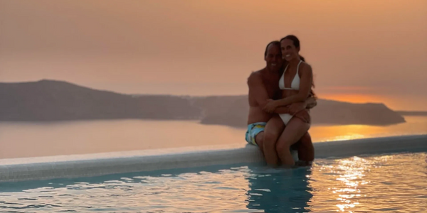 Couple enjoying a sunset by the pool with scenic water and hills in the background.