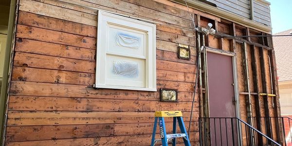 House exterior undergoing renovation with exposed wood and covered furniture.
