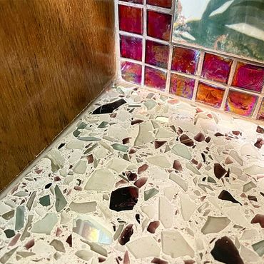 Corner view joining recycled glass countertop, red and green mosaic backsplash, and wood cabinets
