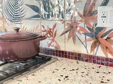 Close up view of glass counter, mosaic backsplash, red border tile, and purple cast iron pot.