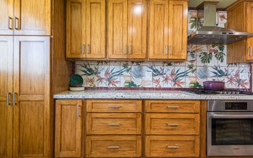 Custom kitchen cabinets with a tropical mosaic backsplash, Bosch appliances, and Le Creuset cookware