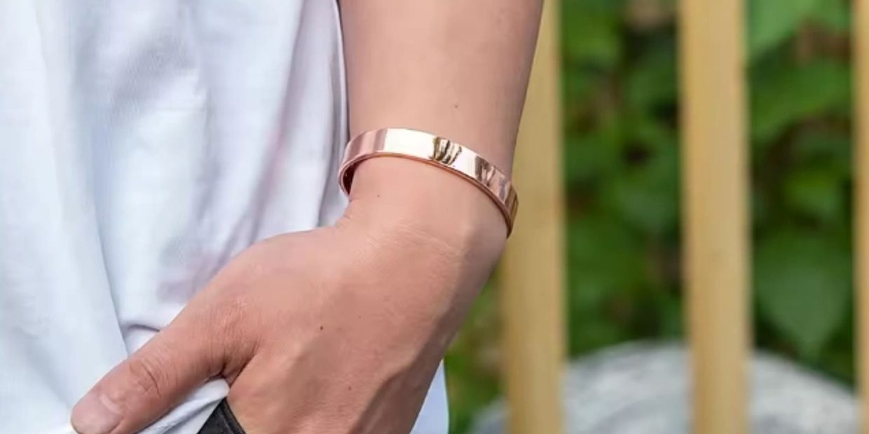 Hand wearing a rose gold bracelet with "Pure Copper" engraved.