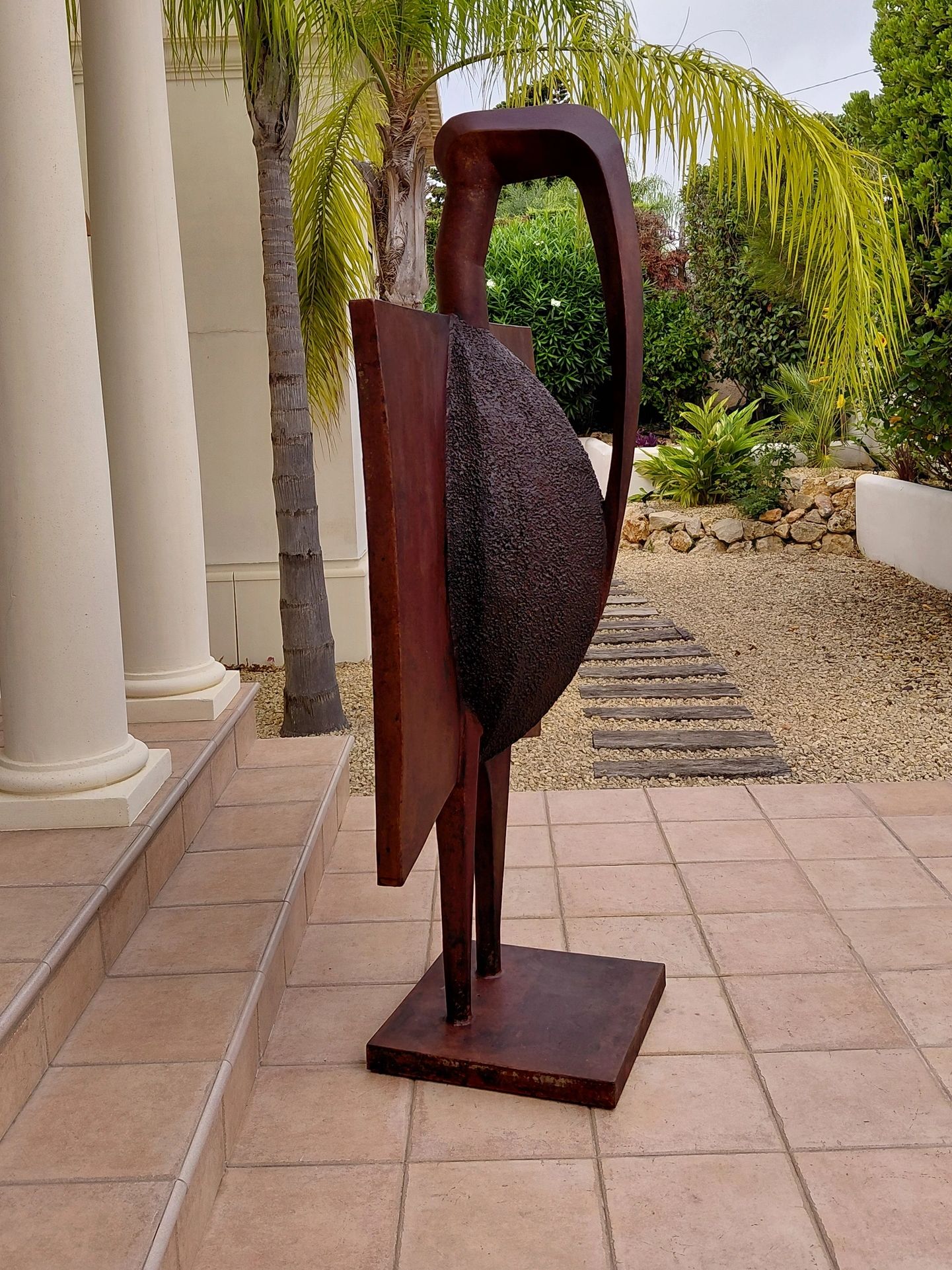 Abstract rust-colored metal sculpture on a tiled patio.