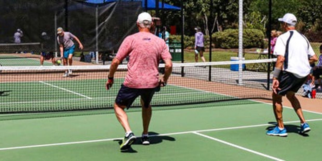 Two men playing pickleball on an outdoor court on a sunny day.