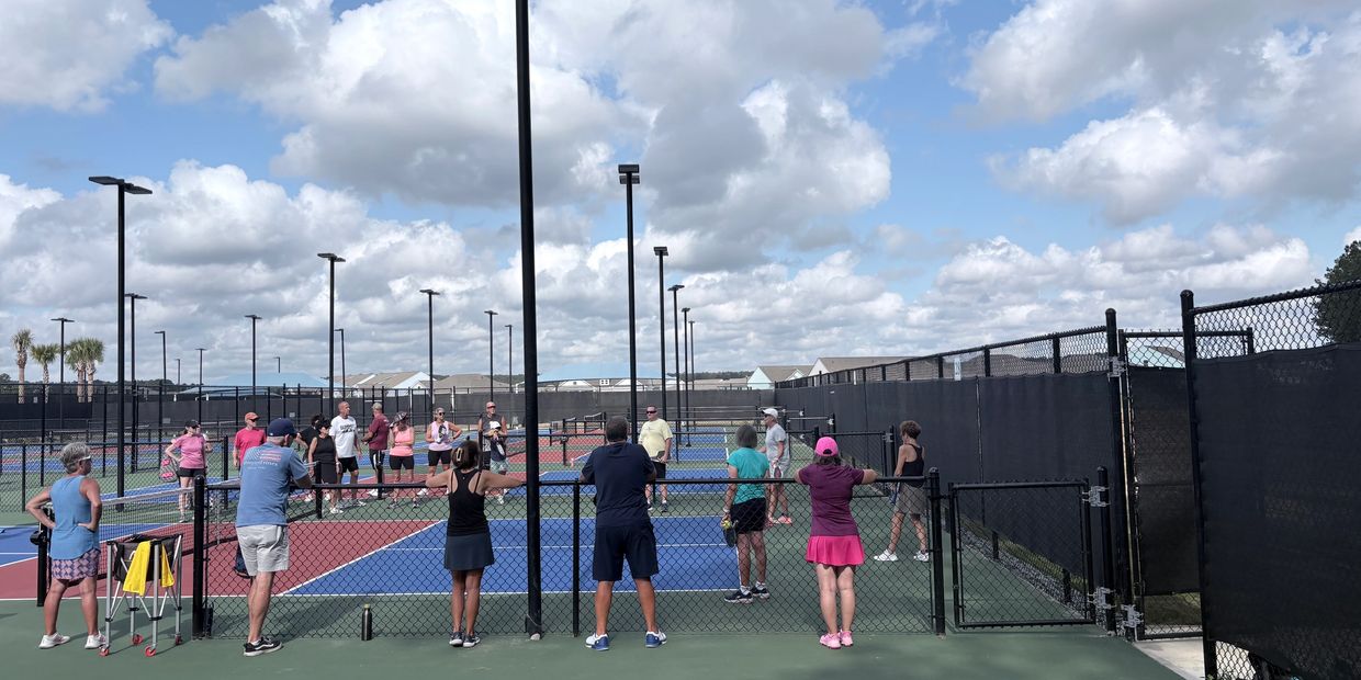 Group of people on outdoor pickleball courts under a cloudy sky.