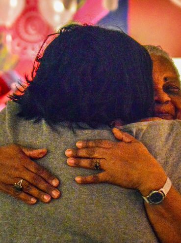 Two people warmly embracing in a colorful, cozy setting.