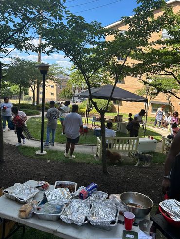 Outdoor gathering with food and people enjoying a sunny day in a neighborhood courtyard.