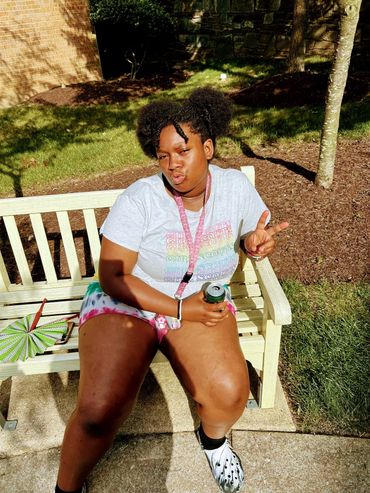A young woman sitting on a bench, making a peace sign with her hand.