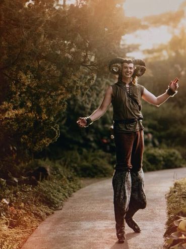 A stilt performer dressed as a faun posing for a photo along a garden path