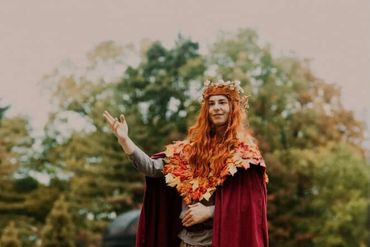 A stilt performer dressed as an autumn elf posing for a photo along a garden path