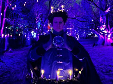A crystal ball juggler wearing a candlelit wreath on his head and another larger one on his waist