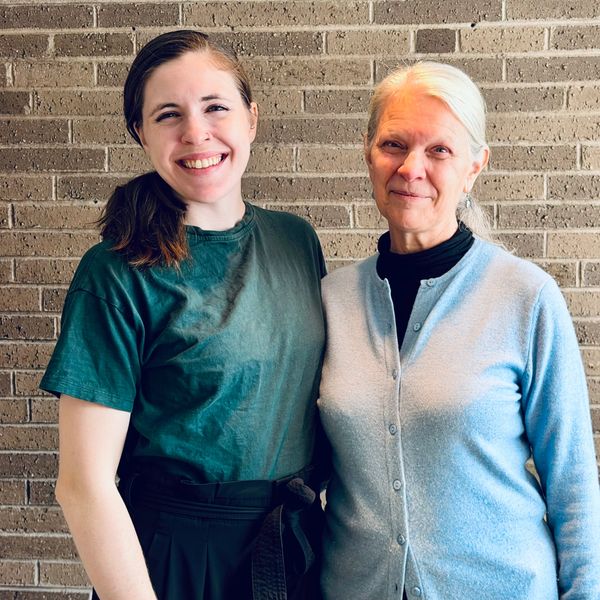 Two women smiling together against a brick wall background.