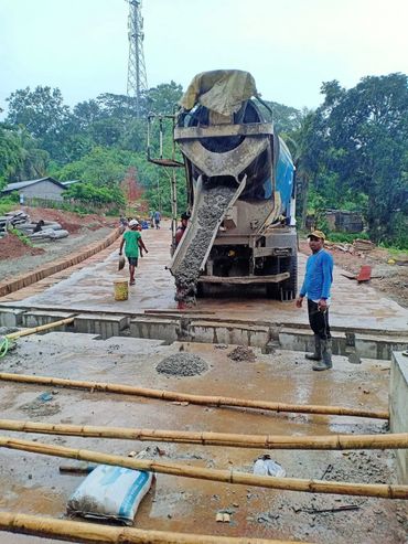 Construction workers pouring concrete from a mixer truck at a rainy site.