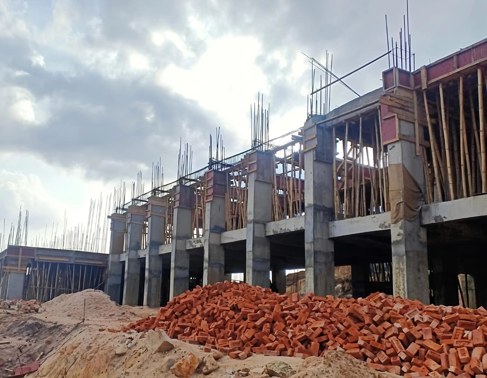 Under-construction building with concrete pillars and piles of red bricks.