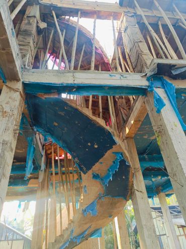 Under-construction spiral staircase with wooden scaffolding and blue protective sheets.