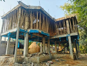 Two-story building under construction with bamboo scaffolding and concrete pillars.