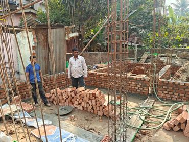 Two men standing at a brick construction site with metal reinforcements.