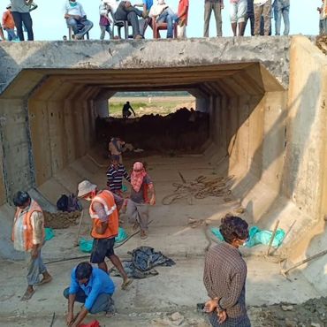 Workers constructing a large concrete drainage tunnel with observers on top.