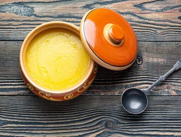 Creamy yellow soup served in a rustic orange bowl with lid and a ladle.