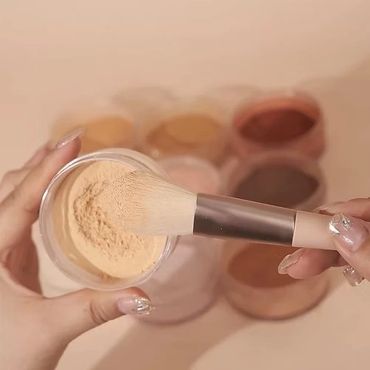 Makeup brush picking up loose powder from a container.