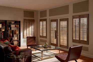 A cozy living room with brown leather chairs and wooden shutters.