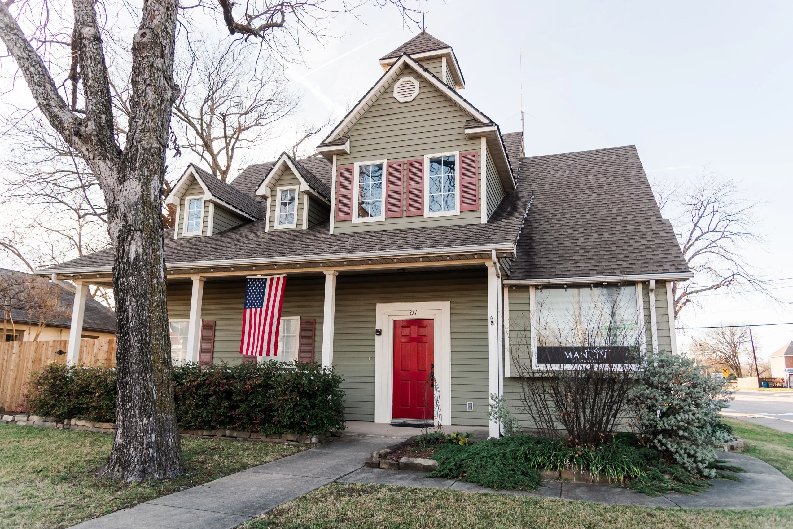 A charming green house with a red door and American flag on the porch.
