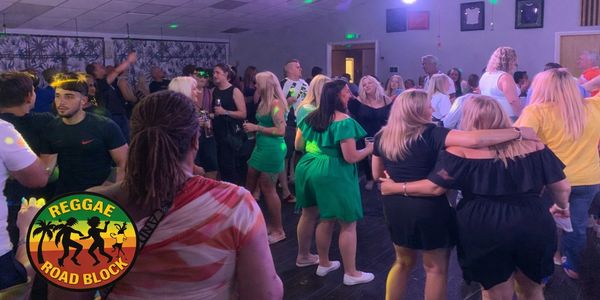 Crowd enjoying a reggae-themed indoor party with colorful lights.