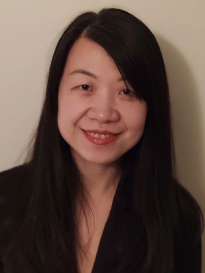 Portrait of a smiling woman with long dark hair against a neutral background.