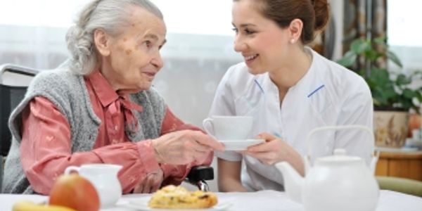 Caregiver serving tea to an elderly woman at home