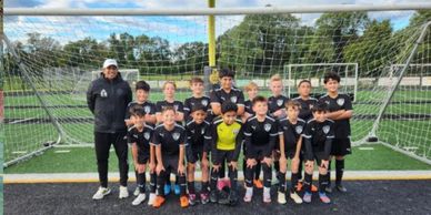 Youth soccer team posing on the field in front of goalpost.