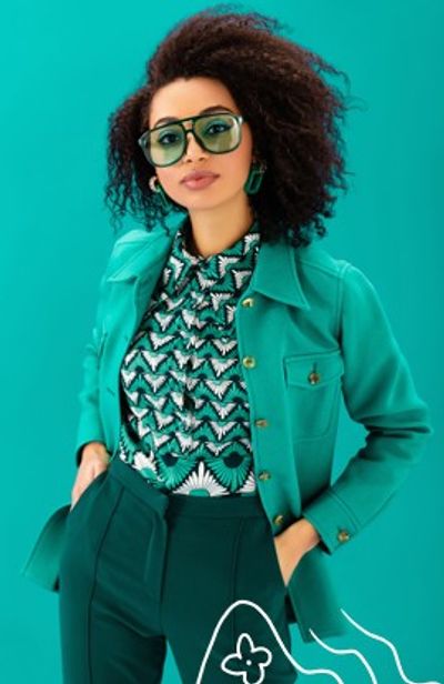 Woman in teal outfit with patterned blouse and large sunglasses.