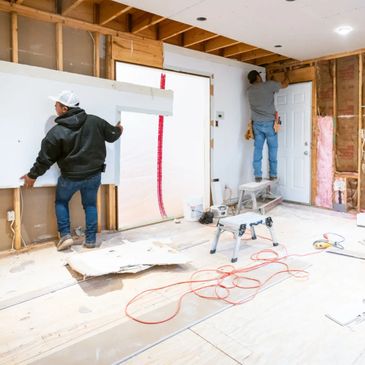 Two workers installing drywall in a room under renovation.