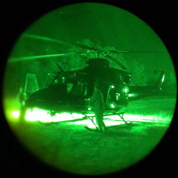 Night vision view of a helicopter on the ground with a person nearby.